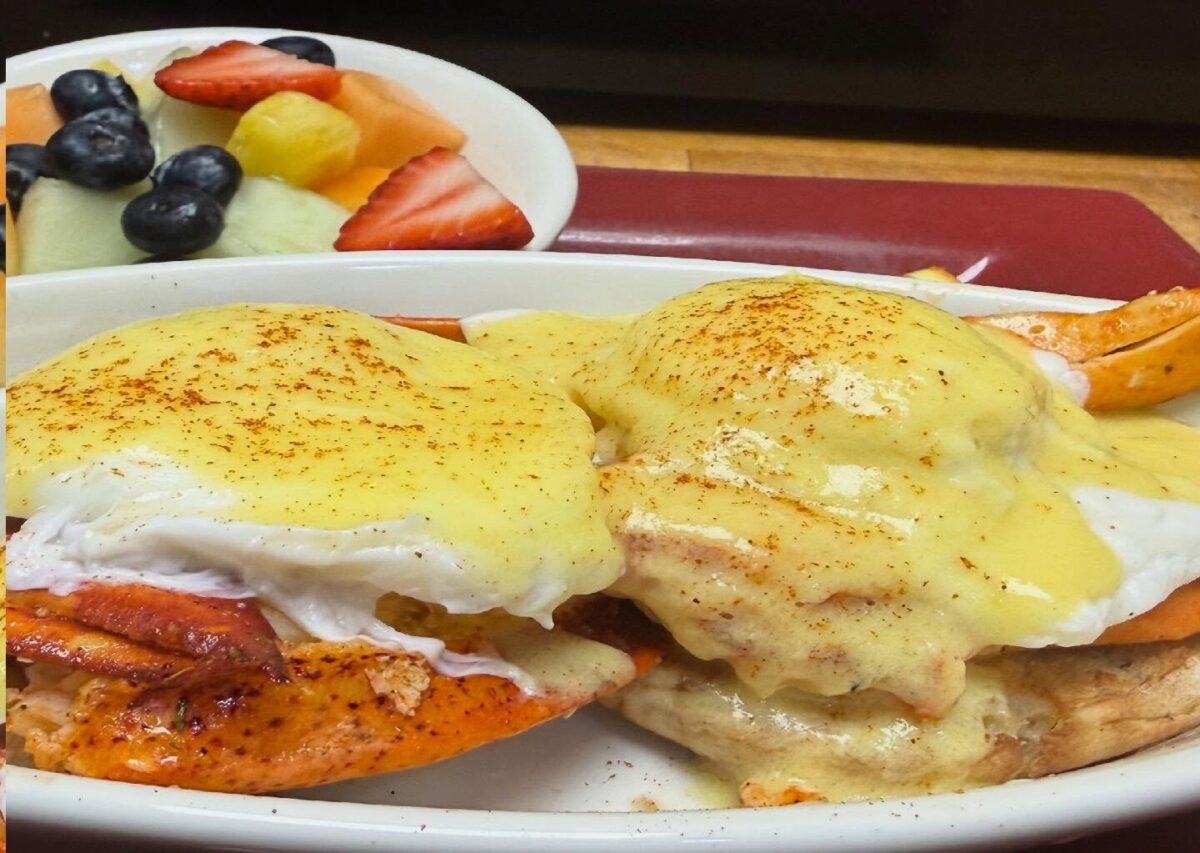 An egg benedict dish served with a side of fruit.